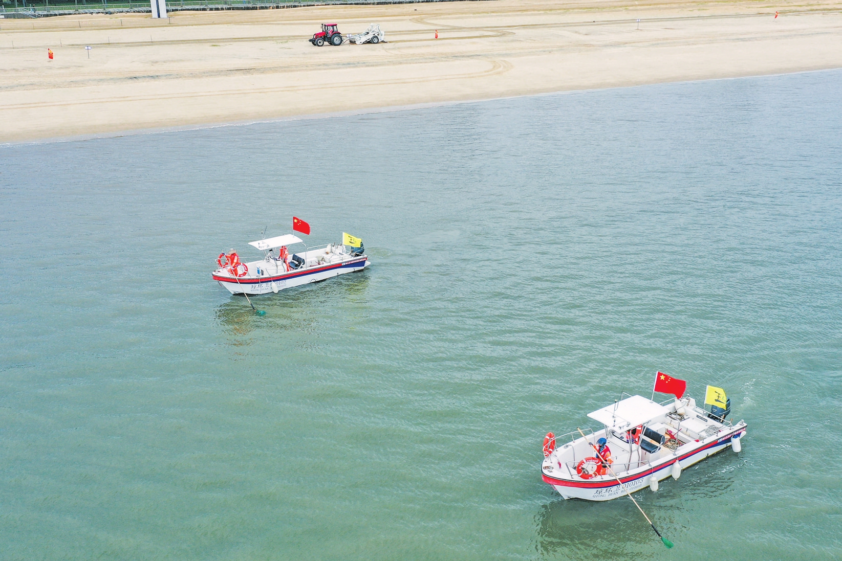 在海口假日海滩,一架无人机在海域上空盘旋,两艘作业船在海上打捞